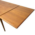 Load image into Gallery viewer, Close-up of a mid-century modern wooden dining table with a warm medium-brown wood grain finish and a visible leaf extension joint, shown on a plain white background.
