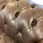 Load image into Gallery viewer, Close-up of a brown tufted leather sofa or chair cushion, showing the leather texture and button tufting details.
