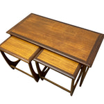 Load image into Gallery viewer, A set of three nested wooden nesting tables with a warm medium-brown wood grain finish and dark brown trim, shown on a plain white background.
