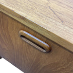 Load image into Gallery viewer, Close-up of a mid-century modern wooden cabinet or desk drawer, showing a curved, recessed metal pull handle integrated into the wood grain.
