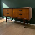 Load image into Gallery viewer, Mid-century modern wooden sideboard with six drawers, dark metal handles, and tapered legs, positioned against a dark green wall on a light wood floor.
