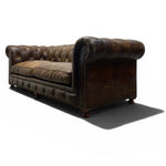 Load image into Gallery viewer, A classic Chesterfield loveseat sofa upholstered in distressed dark brown leather, shown from a three-quarters angle on a white background with a soft shadow.

