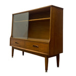 Load image into Gallery viewer, Mid-century modern wooden hutch with a glass door, open shelving, two drawers, and tapered legs, shown on a plain white background.
