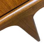 Load image into Gallery viewer, Close-up detail of a mid-century modern wooden furniture piece, showing a warm brown wood grain finish and a sculptural tapered leg against a white background.
