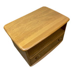 Load image into Gallery viewer, A mid-century modern wooden side table or cabinet with a warm honey-toned wood finish, featuring a rounded rectangular top, a single open shelf, and two round drawer pulls on the front.
