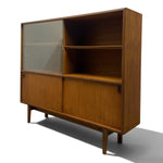 Load image into Gallery viewer, A mid-century modern wooden bookcase with a warm brown wood grain finish, featuring a glass-front cabinet on the left, open shelving in the upper right, and two lower cabinet doors on a white background.
