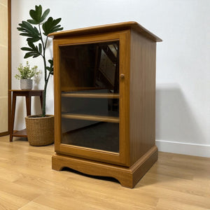 Wooden cabinet with glass doors on a wooden floor with a plant in the background