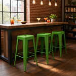 Load image into Gallery viewer, Three bright green metal bar stools positioned in front of a rustic wooden counter in a loft-style bar or cafe with brick walls, hanging bulbs, and cocktail glasses on the counter.
