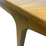 Load image into Gallery viewer, Close-up detail of a wooden table corner showing the warm medium-brown wood grain on the tabletop and apron, with a white background.
