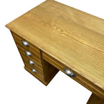 Load image into Gallery viewer, A wooden writing desk with a warm honey finish, featuring a column of three drawers on the left with silver metal pulls and a single open drawer on the right, shown against a plain white background.
