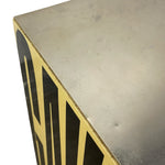Load image into Gallery viewer, Close-up of a square metal table corner showing a brushed silver top surface and a gold side panel with black geometric lettering, photographed on a white background.
