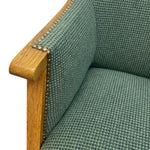 Load image into Gallery viewer, Close-up of a green upholstered chair with wooden armrest and studded detailing.
