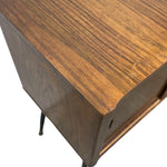 Load image into Gallery viewer, Close-up of a mid-century modern wooden sideboard or cabinet corner, showing a warm brown wood grain finish and slim dark metal legs against a white background.
