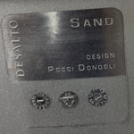 Load image into Gallery viewer, A close-up of a dark gray textured surface featuring a rectangular metal plaque with engraved text reading 'DESALTO SAND DESIGN POCCI DONDOLI' and three small circular dial-like markings below.
