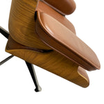 Load image into Gallery viewer, Close-up of a mid-century modern lounge chair with a warm brown wood grain frame and tan leather cushions, including the footrest and part of the black metal legs, set against a solid white background.
