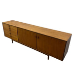 Load image into Gallery viewer, Mid-century modern wooden sideboard with a warm medium-brown wood grain finish, featuring five drawers on the left, two cabinet doors in the center, and tapered legs, shown on a plain white background.
