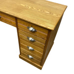 Load image into Gallery viewer, A close-up of a wooden writing desk with a five-drawer pedestal base, featuring a warm oak finish and silver metal drawer pulls, shown on a plain white background.
