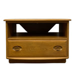 Load image into Gallery viewer, A mid-century modern wooden side table with a warm honey finish, featuring two oval drawer pulls and a triangular cutout in the open back shelf, shown against a plain white background.
