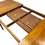 Load image into Gallery viewer, Close-up of a wooden dining table with the top panel lifted open to show the underside, including hinges, support beams, and a brass tension rod mechanism on a white background.
