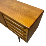 Load image into Gallery viewer, Close-up of a mid-century modern wooden sideboard or credenza, showing the warm honey-toned wood grain, curved drawer fronts, and corner detail against a plain white background.
