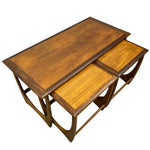 Load image into Gallery viewer, A set of three nested wooden nesting tables with a warm medium-brown finish and distinctive curved metal support legs, shown on a plain white background.
