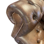 Load image into Gallery viewer, Close-up of a brown tufted leather armrest with decorative nailhead trim, shown against a plain white background.
