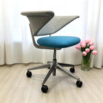 Load image into Gallery viewer, Modern office chair with blue seat and gray backrest on a light wooden floor, next to a vase of pink flowers.
