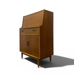 Load image into Gallery viewer, A mid-century modern wooden secretary cabinet with a warm brown wood finish, featuring a slanted top, two drawers, and two cabinet doors with dark metal handles, shown on a white background with a soft shadow.
