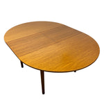 Load image into Gallery viewer, An oval wooden dining table with a warm honey-brown wood grain finish and slim dark legs, shown on a plain white background.
