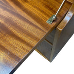 Load image into Gallery viewer, Close-up of a wooden table or cabinet corner showing a warm brown wood grain surface, a metal hinge, and part of the frame against a white background.

