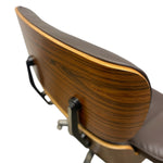 Load image into Gallery viewer, Close-up of a mid-century modern lounge chair showing the backrest with a dark brown wood grain finish, a dark brown leather cushion, and black metal support brackets against a white background.
