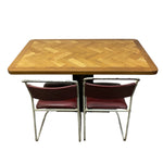 Load image into Gallery viewer, A mid-century modern dining table set featuring a rectangular wooden table with a herringbone patterned top and two matching chairs with burgundy leather seats and chrome metal frames, shown against a plain white background.
