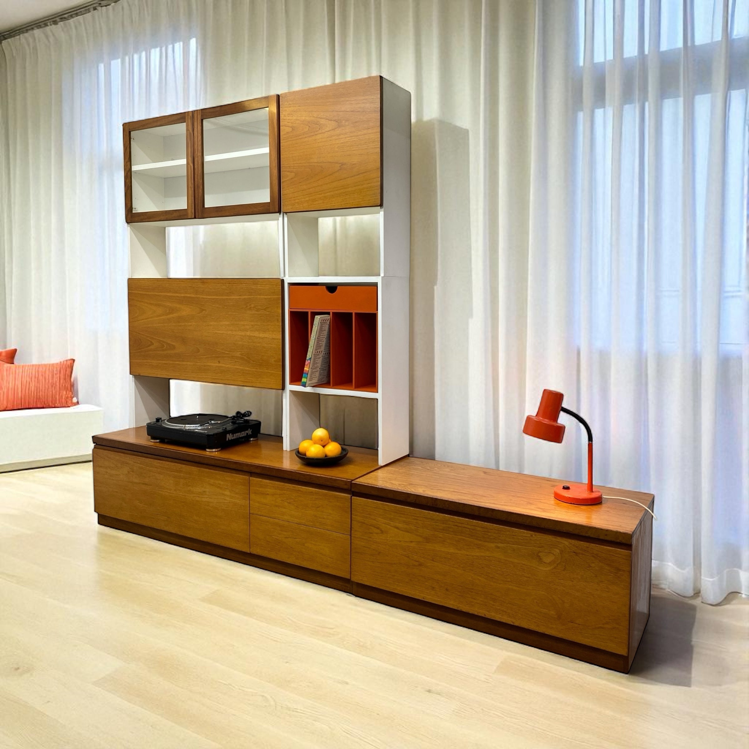 Wooden entertainment console with glass panels and a lamp in a room with white curtains.