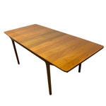 Load image into Gallery viewer, A mid-century modern wooden dining table with a warm medium-brown wood grain finish and tapered dark legs, shown on a plain white background.
