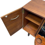 Load image into Gallery viewer, A close-up of a mid-century modern wooden cabinet with its door open, showcasing a warm brown wood grain finish, brass hinges, and a curved metal pull handle.
