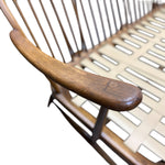 Load image into Gallery viewer, Close-up of a mid-century modern wooden chair with a curved armrest, spindle backrest, and light-colored woven seat slats.
