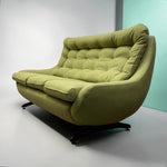 Load image into Gallery viewer, A mid-century modern upholstered lounge chair in olive green fabric with a tufted backrest and dark wooden swivel legs, photographed in a studio setting.
