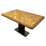 Load image into Gallery viewer, A rectangular wooden dining table with a herringbone-patterned wood top and a black metal pedestal base, shown on a plain white background.
