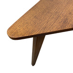 Load image into Gallery viewer, Close-up of a mid-century modern wooden table corner, showing a triangular tabletop with a warm medium-brown wood grain finish and a tapered wooden leg on a white background.
