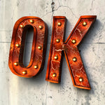 Load image into Gallery viewer, Decorative marquee-style letters 'O' and 'K' in a cracked orange-red metallic finish with small gold light bulbs, mounted against a light concrete wall.
