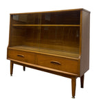 Load image into Gallery viewer, Mid-century modern wooden display cabinet with glass doors, two lower drawers, and tapered legs, shown on a plain white background.
