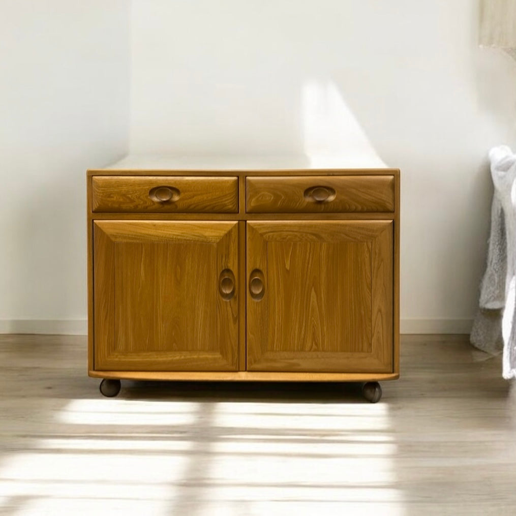 Wooden cabinet with two doors and a drawer on wheels in a room setting.