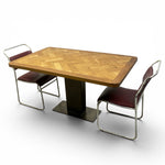 Load image into Gallery viewer, A mid-century modern dining table set featuring a rectangular wooden table with a herringbone pattern top and a dark pedestal base, accompanied by two chrome-framed chairs with burgundy upholstered seats, shown on a white background.
