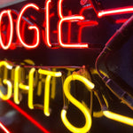 Load image into Gallery viewer, Neon sign with red and yellow letters on a dark background

