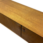 Load image into Gallery viewer, Close-up of a mid-century modern wooden sideboard or credenza with a warm honey-brown wood grain finish and small dark metal handles, shown against a plain white background.
