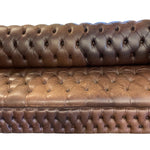 Load image into Gallery viewer, A close-up of a brown tufted leather sofa, showing the detailed button-tufted upholstery and stitching on the backrest and seat, set against a plain white background.
