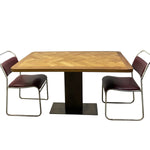 Load image into Gallery viewer, A vintage-style dining table set featuring a rectangular table with a herringbone wood top and a black pedestal base, accompanied by two modern chairs with dark burgundy seats and chrome frames, set against a plain white background.
