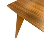 Load image into Gallery viewer, Close-up of a mid-century modern wooden table corner showing the wood grain tabletop and tapered wooden leg against a white background.

