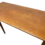 Load image into Gallery viewer, A close-up of a mid-century modern wooden dining table with a warm medium-brown finish and visible wood grain, showing a leaf extension seam on the tabletop.
