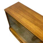 Load image into Gallery viewer, Close-up of a mid-century modern wooden display cabinet with a warm golden-brown wood grain finish and a glass front door, shown against a plain white background.
